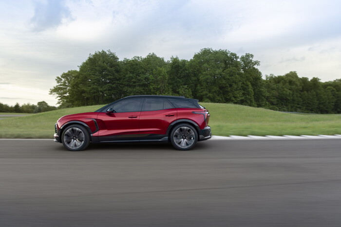 2024 Chevrolet Blazer EV SS in Radiant Red Tintcoat driving on a road with trees. Preproduction mode