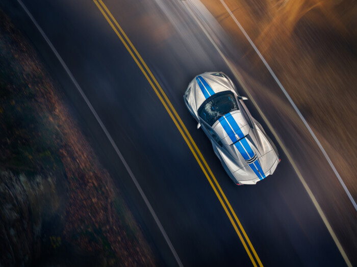 Overhead view of 2024 Chevrolet Corvette E-Ray 3LZ convertible in Silver Flare with Electric Blue stripe package driving on a road. Pre-production model shown. Actual production model may vary. Model year 2024 Corvette E-Ray available 2023.