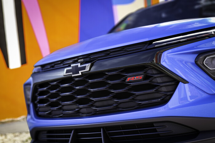 Close up view of grille and badge on 2024 Chevrolet Trailblazer RS in Fountain Blue parked in front of a building. Preproduction model shown. Actual production model may vary. Available in fall 2023.