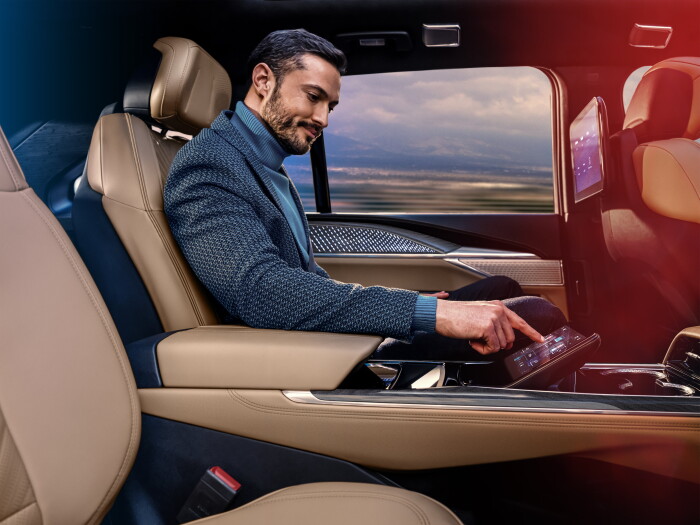 Man sitting in Executive Second Row of Cadillac ESCALADE IQ Sport using the rear command control screen.